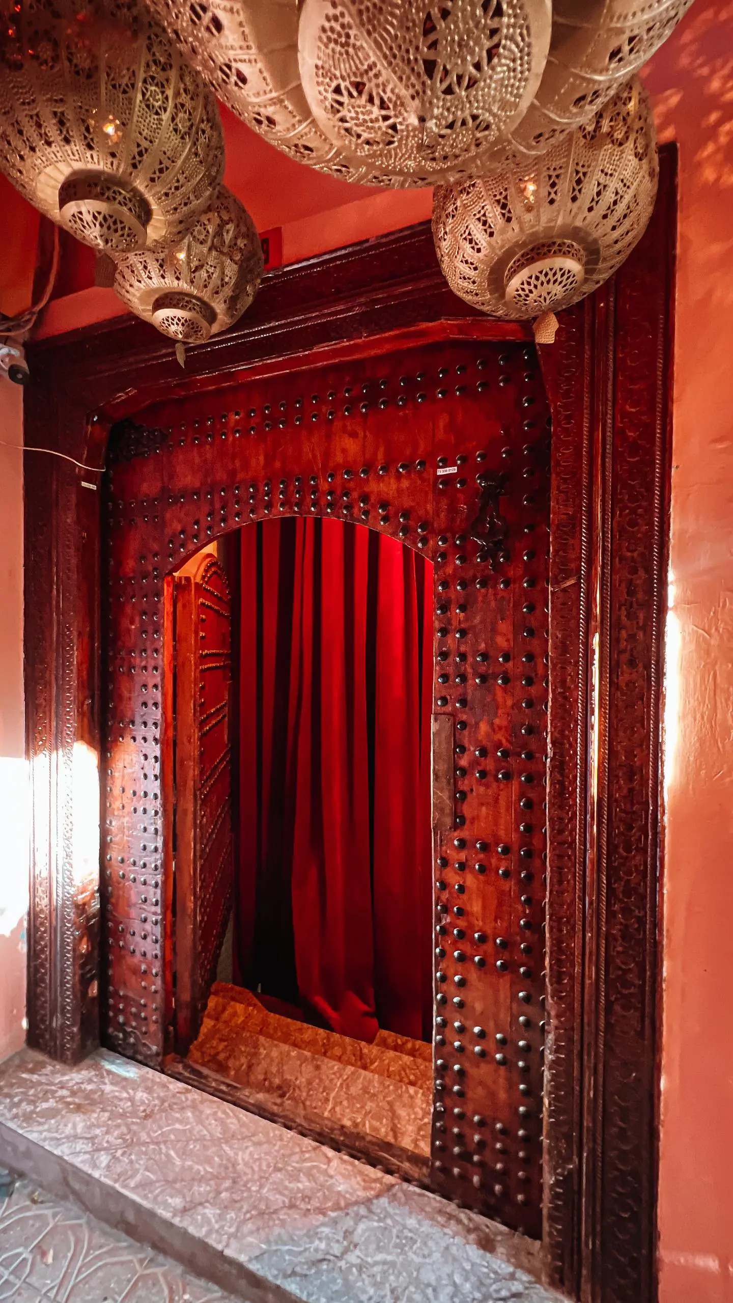La porte rouge cloutée du riad, entrouverte sur un rideau pourpre